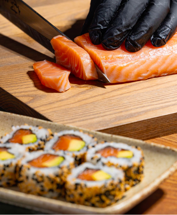 Salmon being sliced and made into sushi rolls